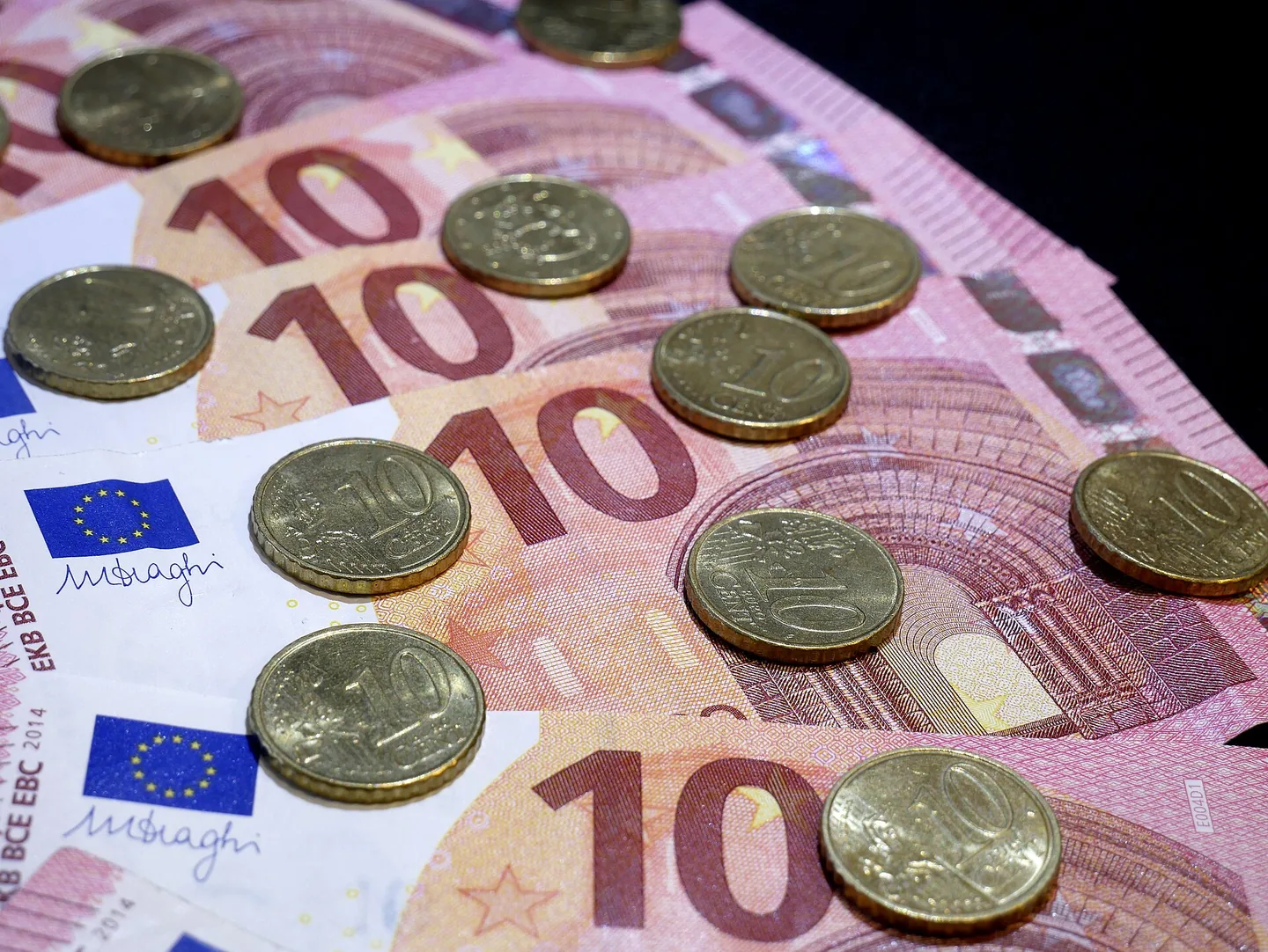 Een close-up van meerdere roze briefjes van 10 euro, met daarover verspreid een aantal gouden muntjes van 10 eurocent.
